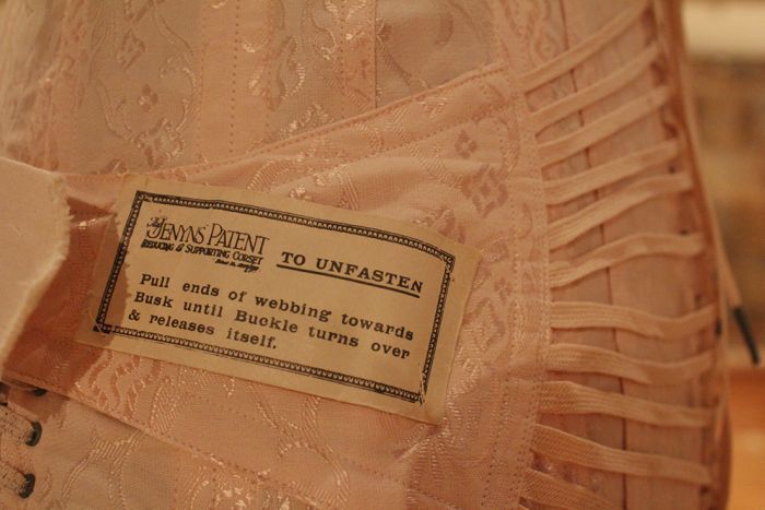 A pink corset strap with an instruction panel sewn on to one of the straps.